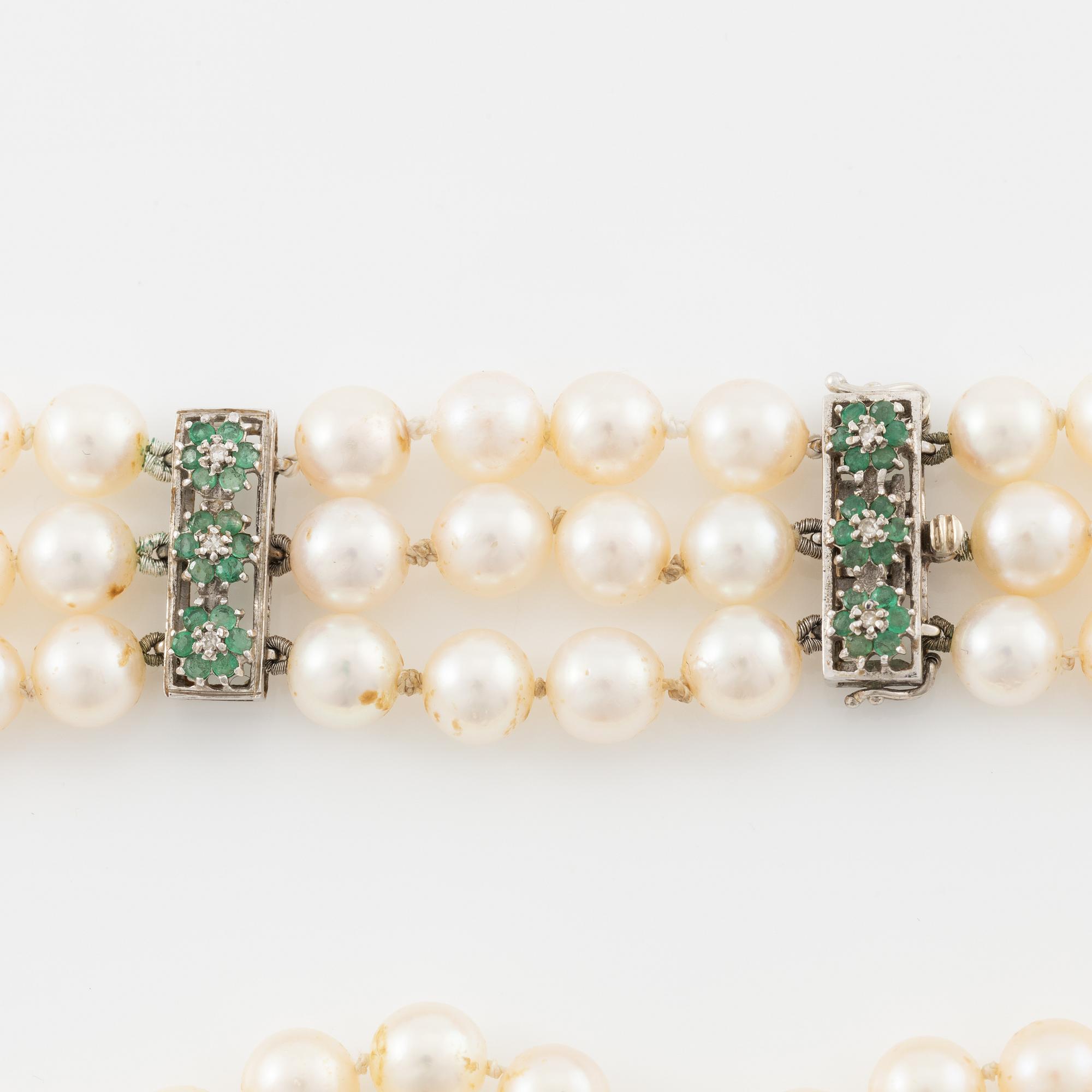 A three strand cultured pearl necklace, clasp in 18K gold with white stones and emeralds.