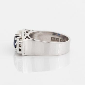 An 18K white gold ring set with a faceted sapphire, possibly synthetic, and round brilliant-cut diamonds.