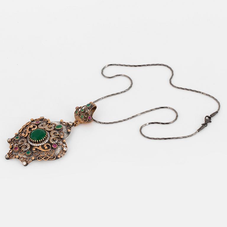 A silver necklace with red, green and colourless stones.