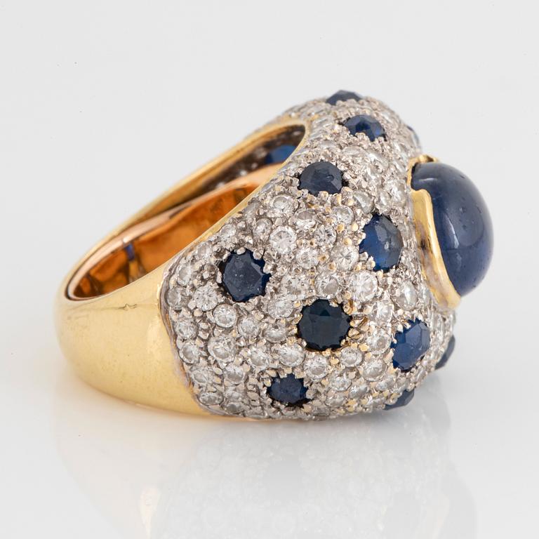 An 18K gold ring set with a cabochon-cut sapphire and round brilliant-cut diamonds and faceted sapphires.