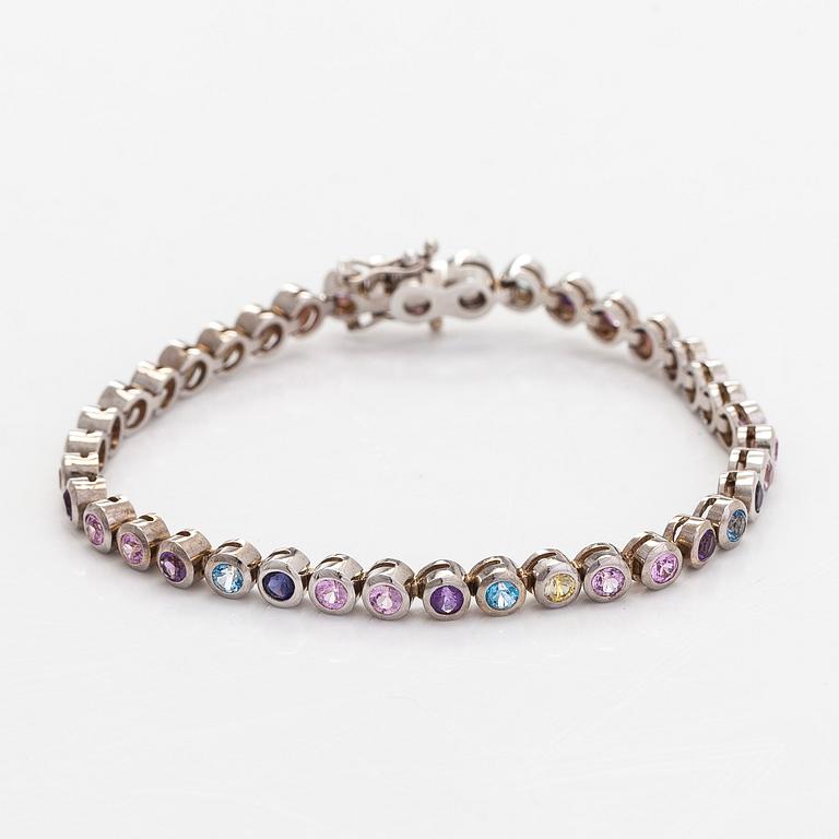 Rannekoru, 18K valkokultaa ja monivärisiä kiviä.