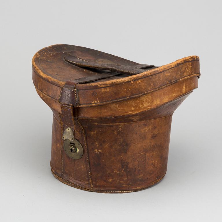 A LEATHER HAT BOX WITH A TOP HAT, 19th century latter part / turn of the century 1900.