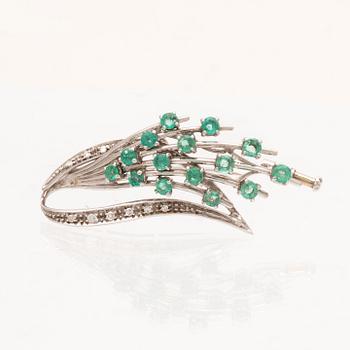 An 18K white gold brooch with round brilliant cut emeralds and single cut diamonds.