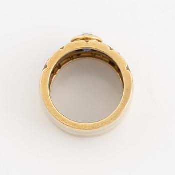 An 18K gold ring set with a faceted sapphire and round brilliant-cut diamonds.