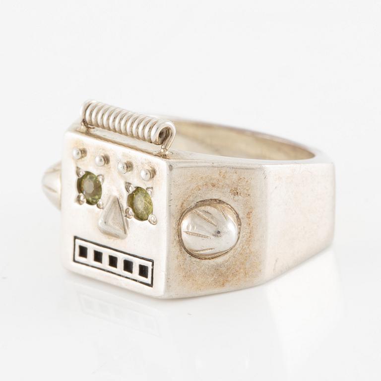Maria Nilsdotter ring i form av ett robothuvud, sterlingsilver och gröna ögon.