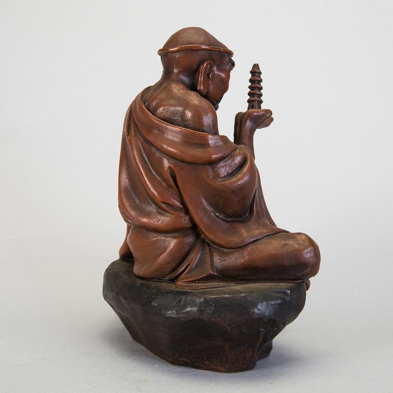 A Japanese earthenware seated figure of a man holding a pagoda, 20th century.