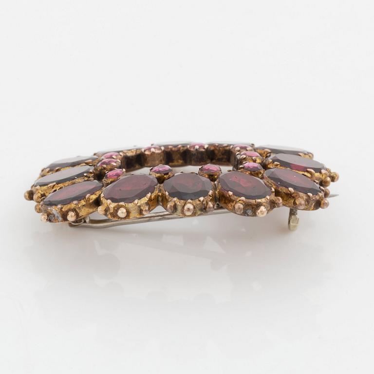 A silver and gold brooch set with faceted garnets.