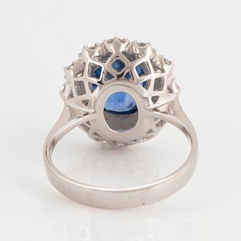 An 18K white gold ring set with a faceted sapphire and round brilliant-cut diamonds.