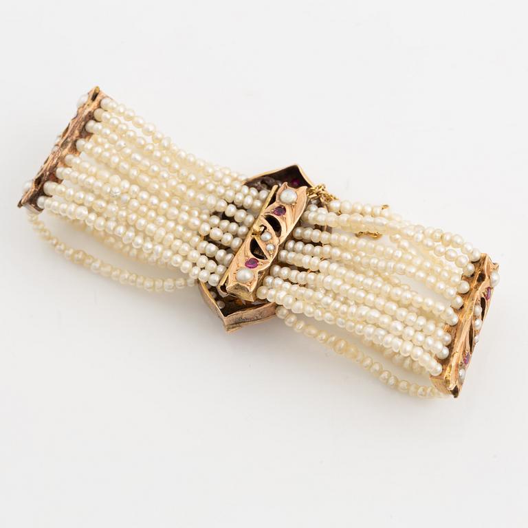 Armband, guld, åtta-radigt med seedpärlor och rubiner.