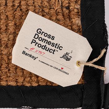 Banksy, dörrmatta, handbroderad med material från livvästar, 2019.