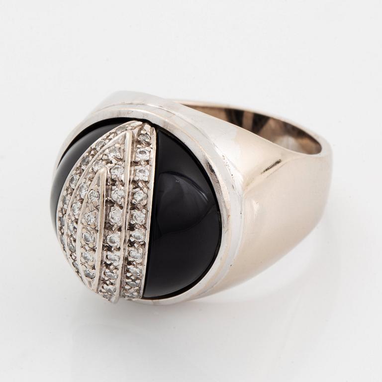 An 18K white gold and onyx ring set with round brilliant-cut diamonds.