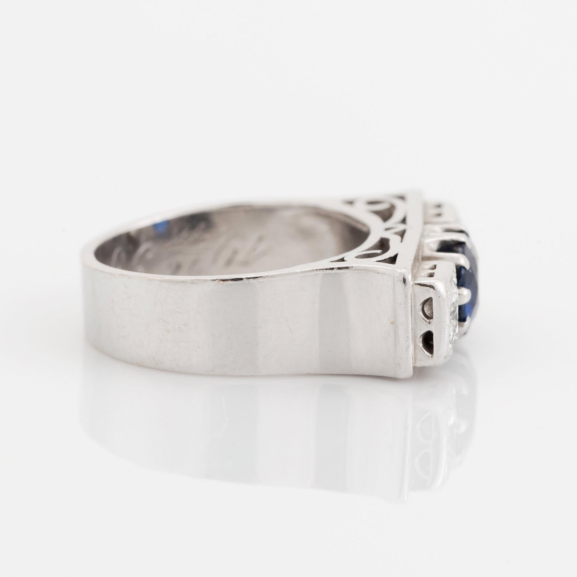 An 18K white gold ring set with a faceted sapphire, possibly synthetic, and round brilliant-cut diamonds.