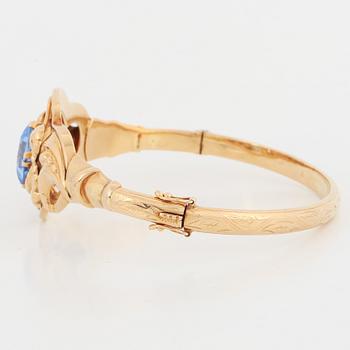 An 18K gold bangle set with a blue synthetic stone.