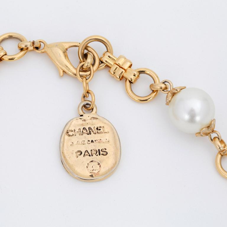 CHANEL, a gold colored necklace with decorative white pearls.