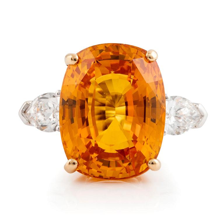 An 18K white gold ring set with a cushion shaped orange-yellow sapphire.