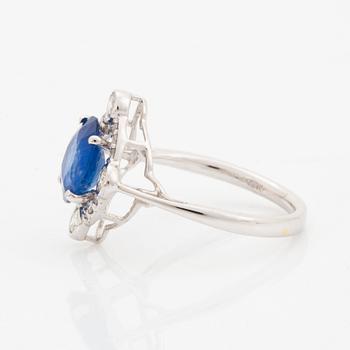An 18K white gold ring set with a faceted sapphire and round brilliant-cut diamonds.