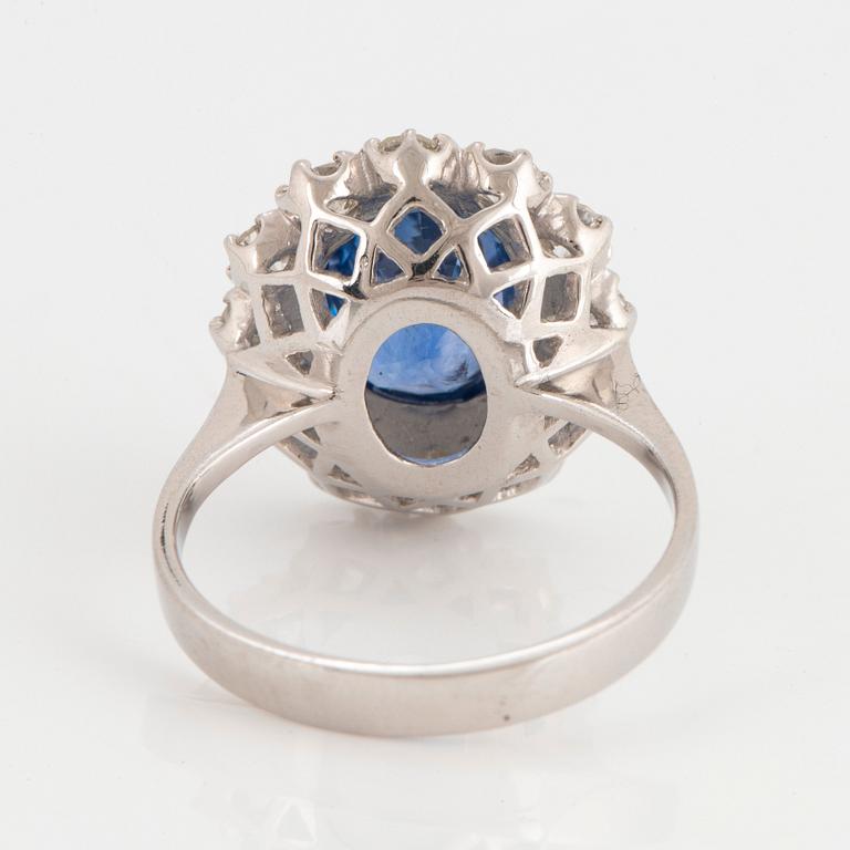 An 18K white gold ring set with a faceted sapphire and round brilliant-cut diamonds.