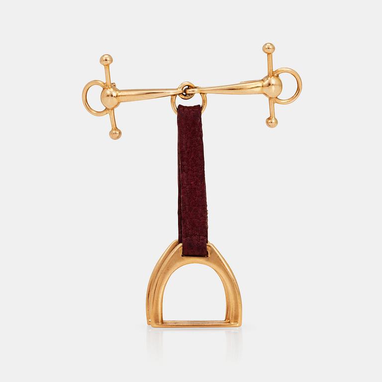 A stirrup and bridle brooch with leather details.
