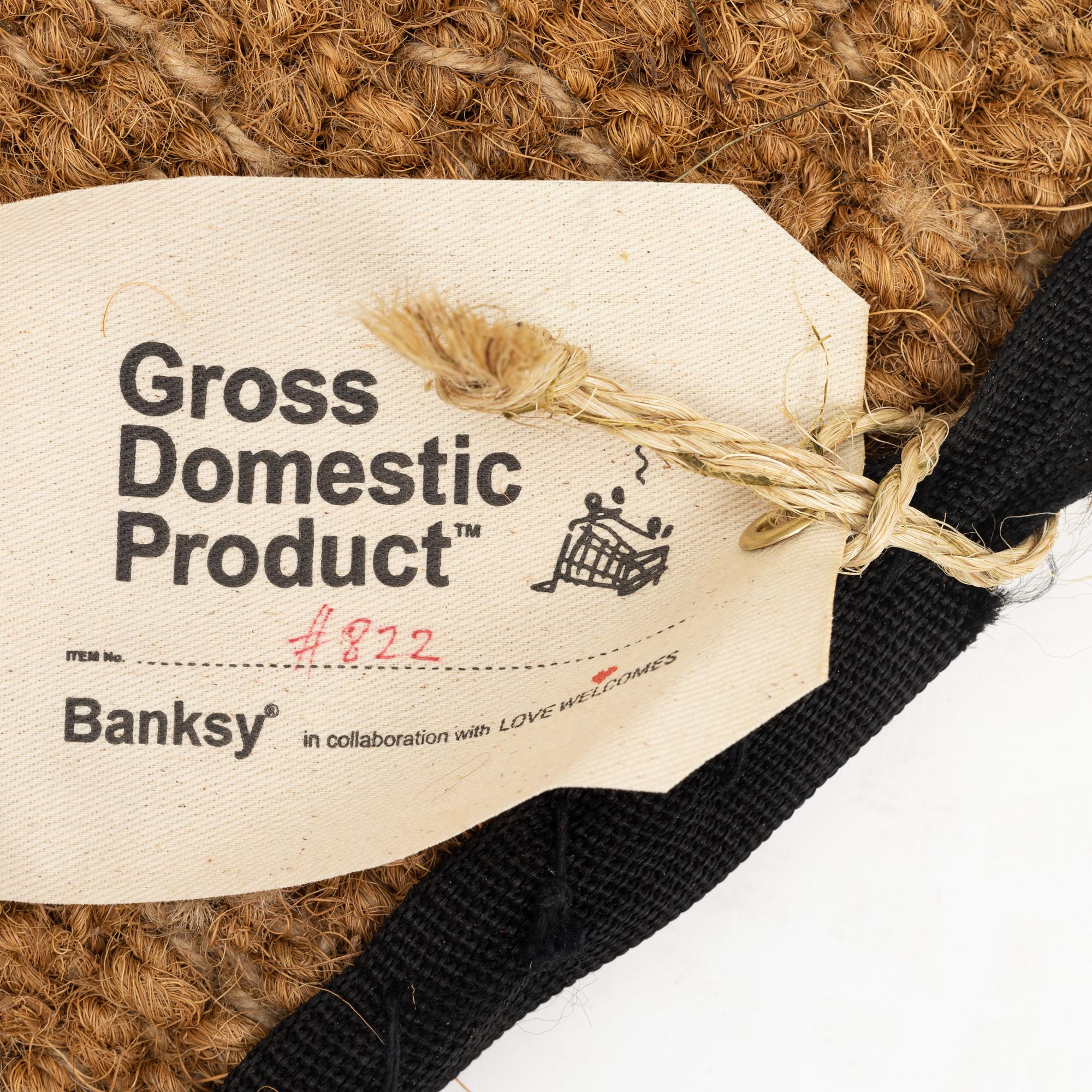 Banksy, dörrmatta, handbroderad med material från livvästar, 2019.