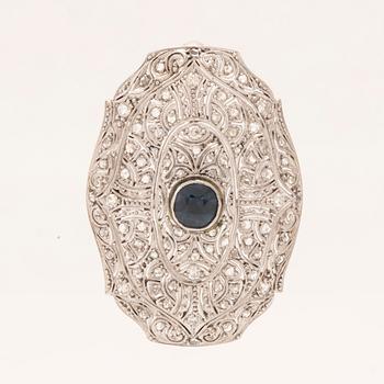 An 18K white gold brooch set with a facet-cut sapphire possibly synthetic, as well as brilliant and rose-cut diamonds.