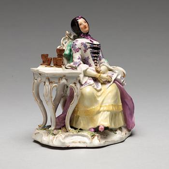 A Meissen porcelain figure of a lady by a table.