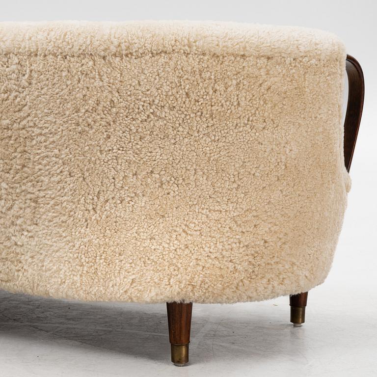 A curved sofa attributed to Viggo Boesen with new sheepskin upholstery and stained beech tree armrests.