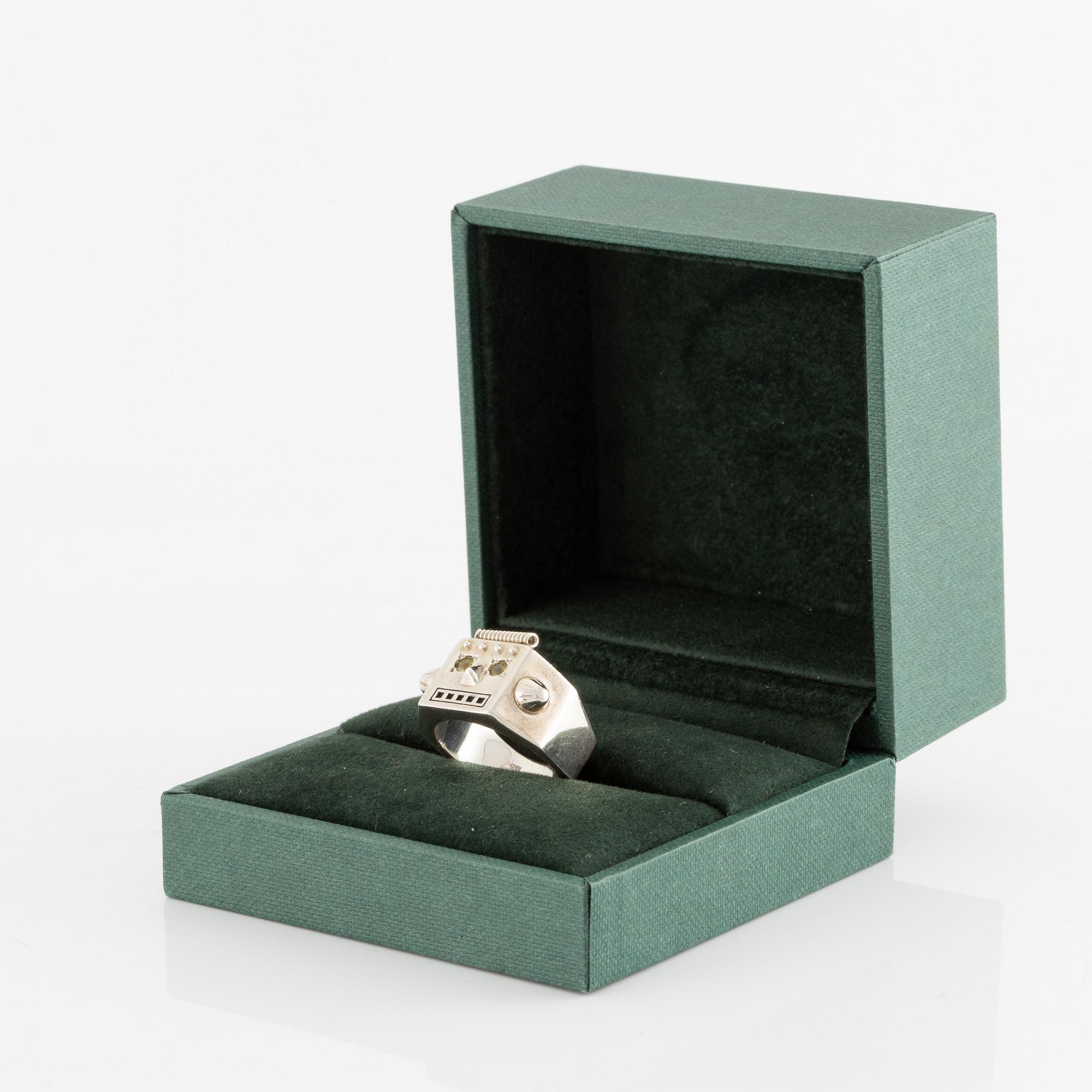 Maria Nilsdotter ring i form av ett robothuvud, sterlingsilver och gröna ögon.