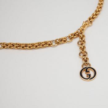 GUCCI, a gold colored mongrammed chain.