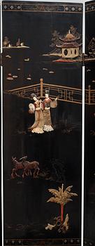 A chinese black lacquer six-panel screen, early 20th Century, with figures in gardens, inlays of carved mother of pearl, coloured bone, tree, and different stones. Back of panels with flowers painted in gold.