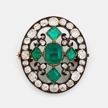 A gold and silver brooch set with faceted emeralds and old- and rose-cut diamonds.