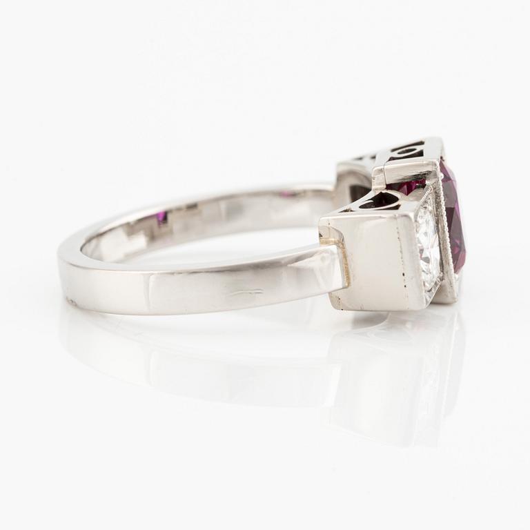 A platinum ring with a faceted ruby and two round brilliant-cut diamonds.