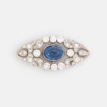 A platinum brooch set with a cabochon-cut sapphire and a cabochon-cut emerald.