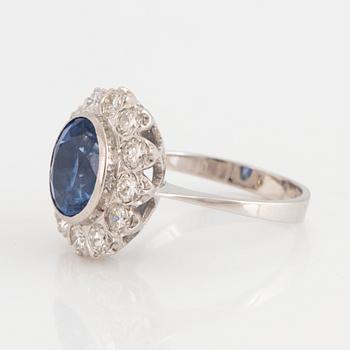 An 18K white gold ring set with a faceted sapphire and round brilliant-cut diamonds.