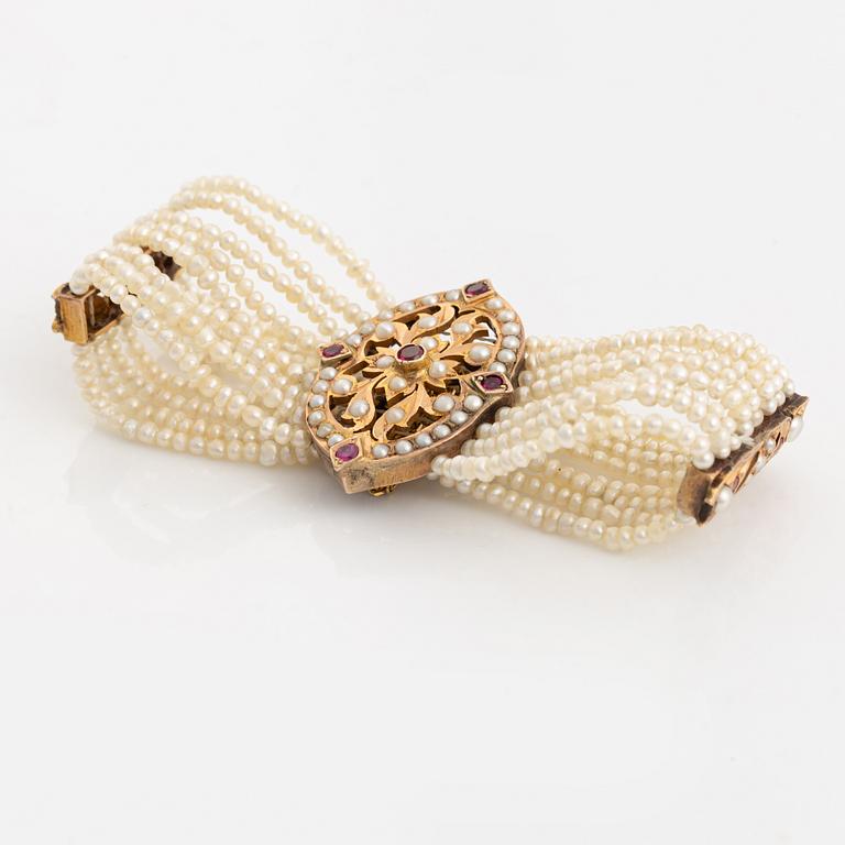 Armband, guld, åtta-radigt med seedpärlor och rubiner.