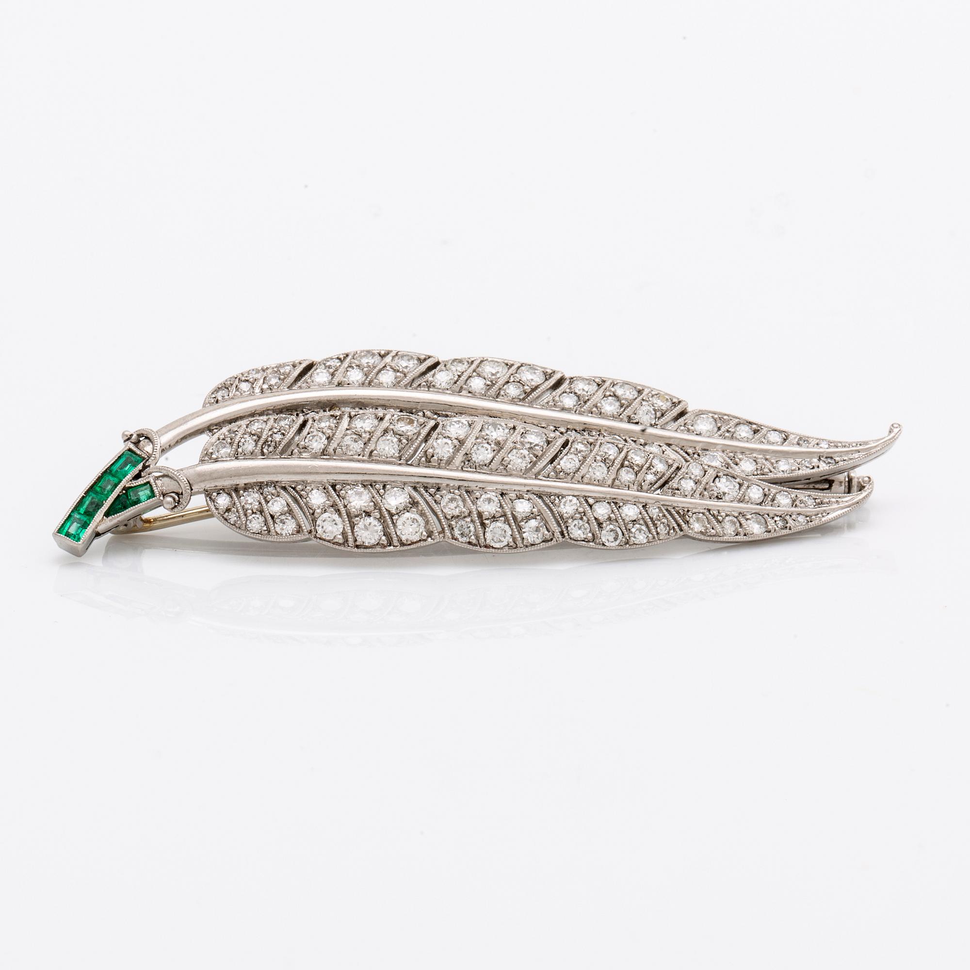 A platinum brooch set with round brilliant-cut diamonds and emeralds.