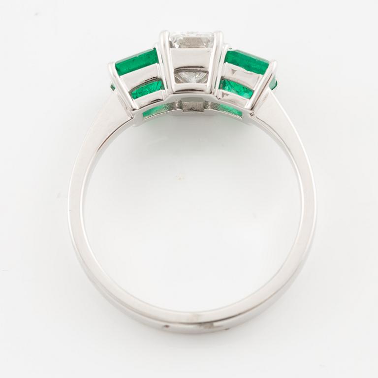 An 18K white gold ring set with an emerald-cut diamond and two step-cut emeralds.