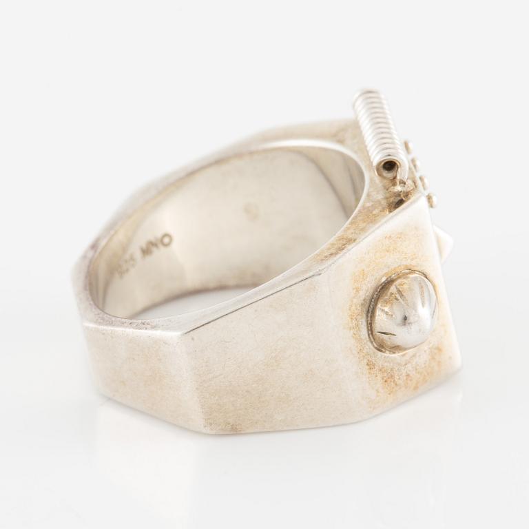 Maria Nilsdotter ring i form av ett robothuvud, sterlingsilver och gröna ögon.
