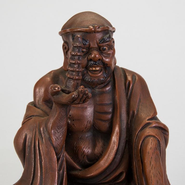 A Japanese earthenware seated figure of a man holding a pagoda, 20th century.