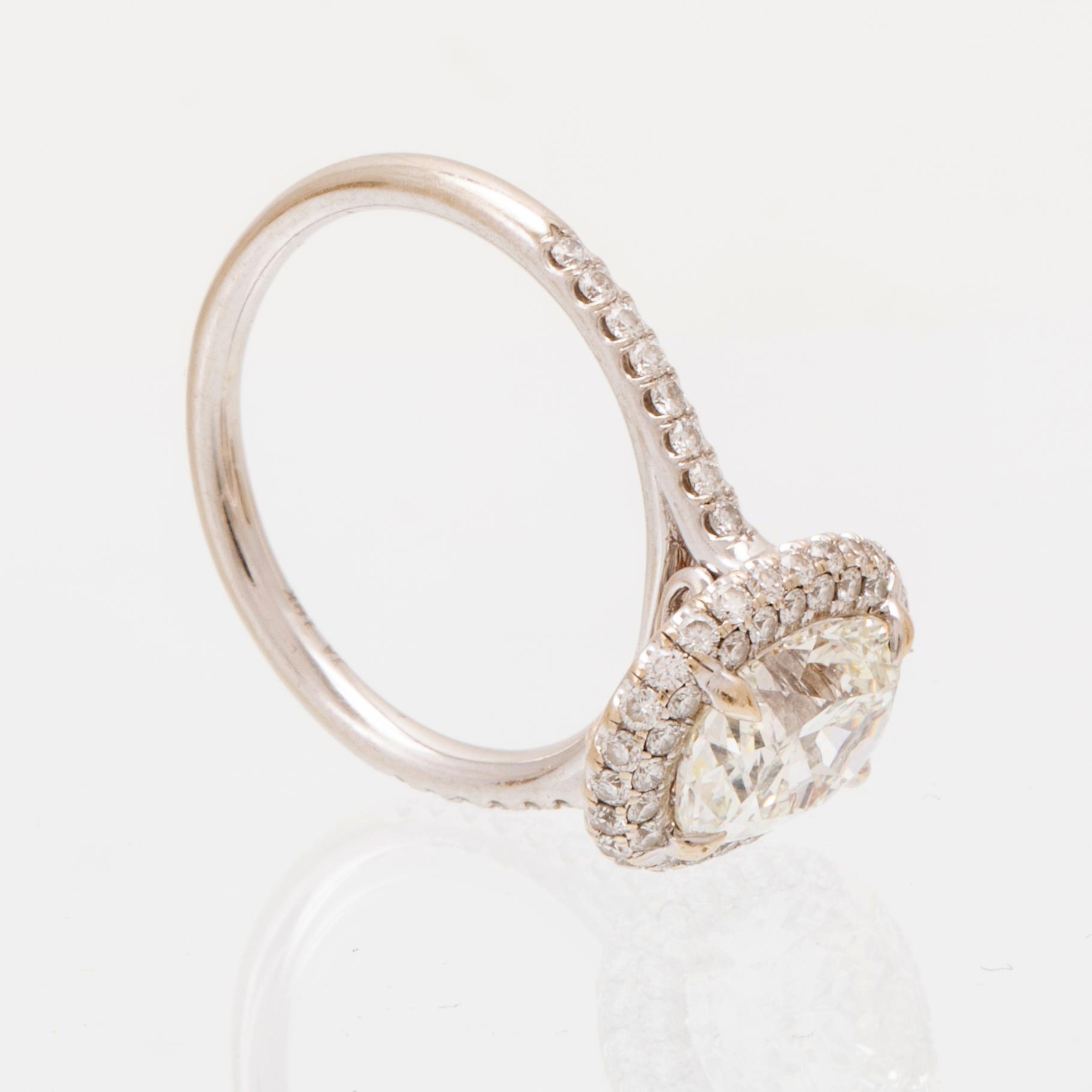 An 18K white gold ring by James Allen, set with an oval brilliant cut diamond in a halo of round brilliant cut diamonds.