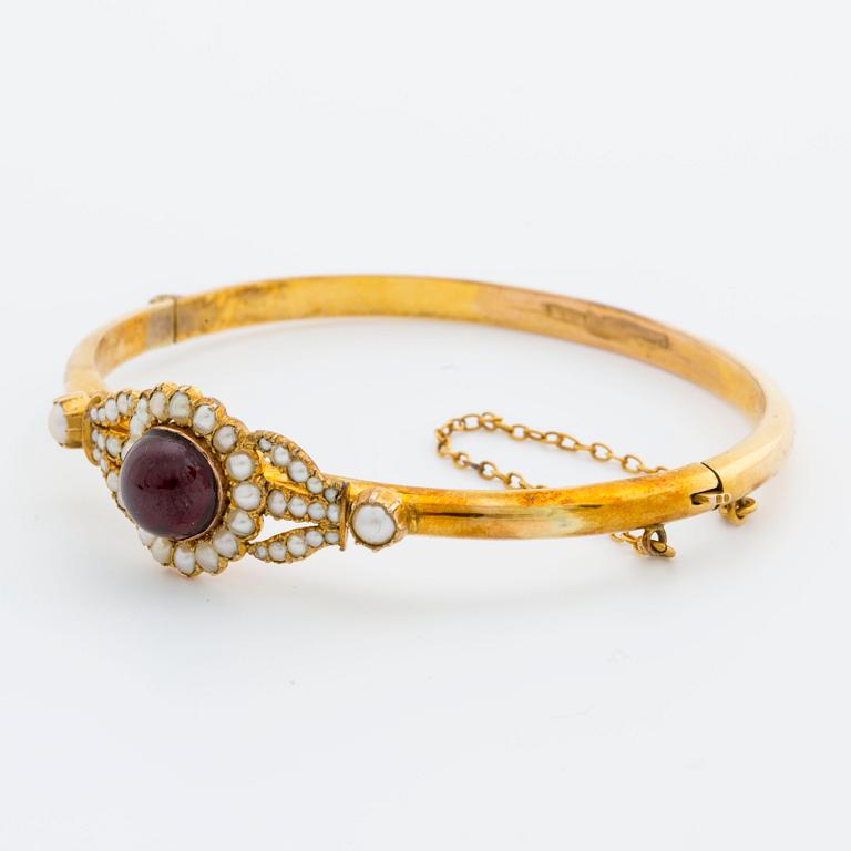 BANGLE, 10K gold, 1 cabochon garnet and seed pearls. 1900s. Hinged mechanism.