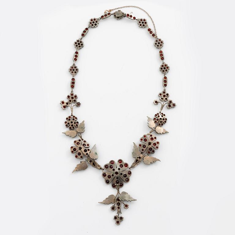 Garniture, necklace/bracelet and earrings in silver with garnets in the form of floral motifs, around the turn of the 20th century.