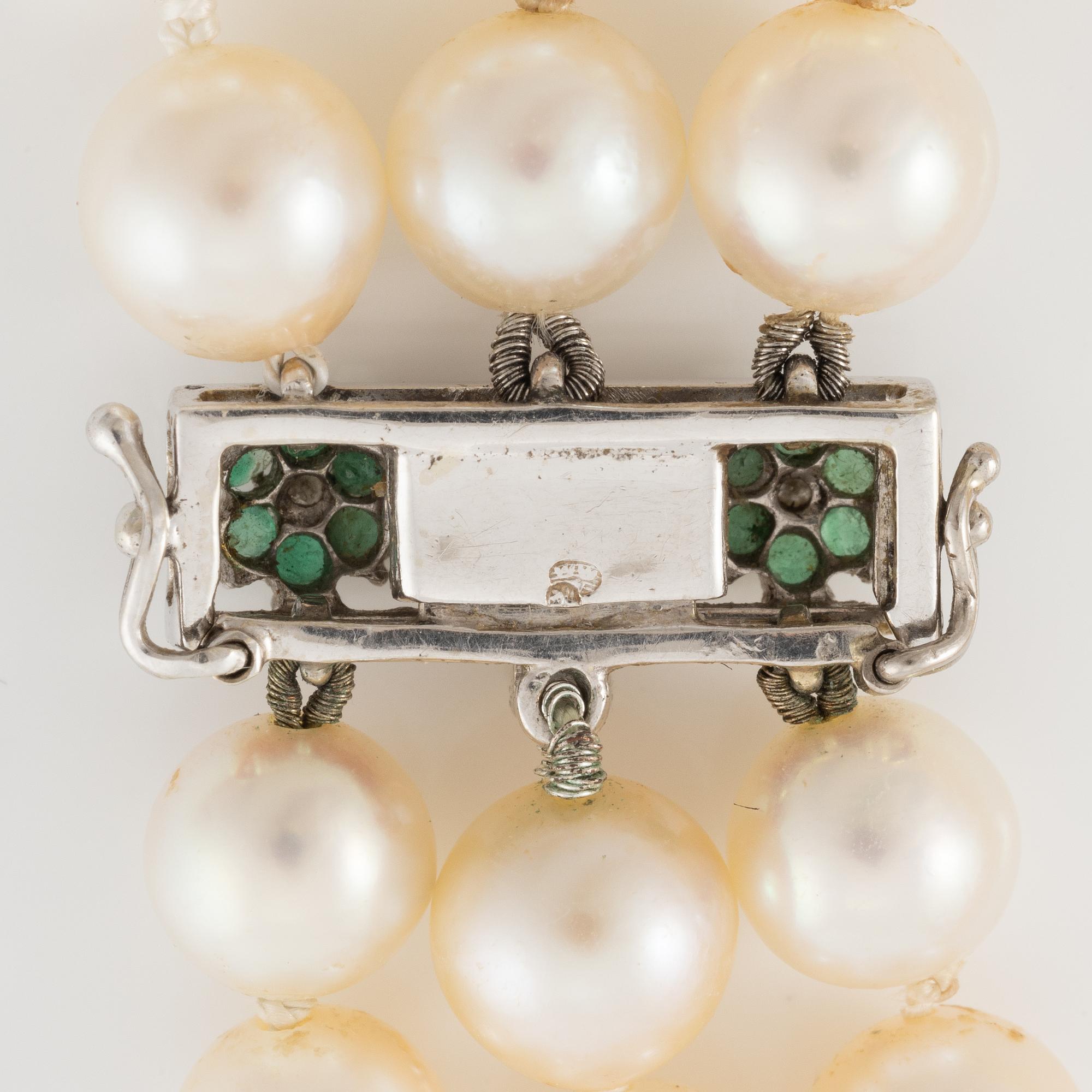 A three strand cultured pearl necklace, clasp in 18K gold with white stones and emeralds.