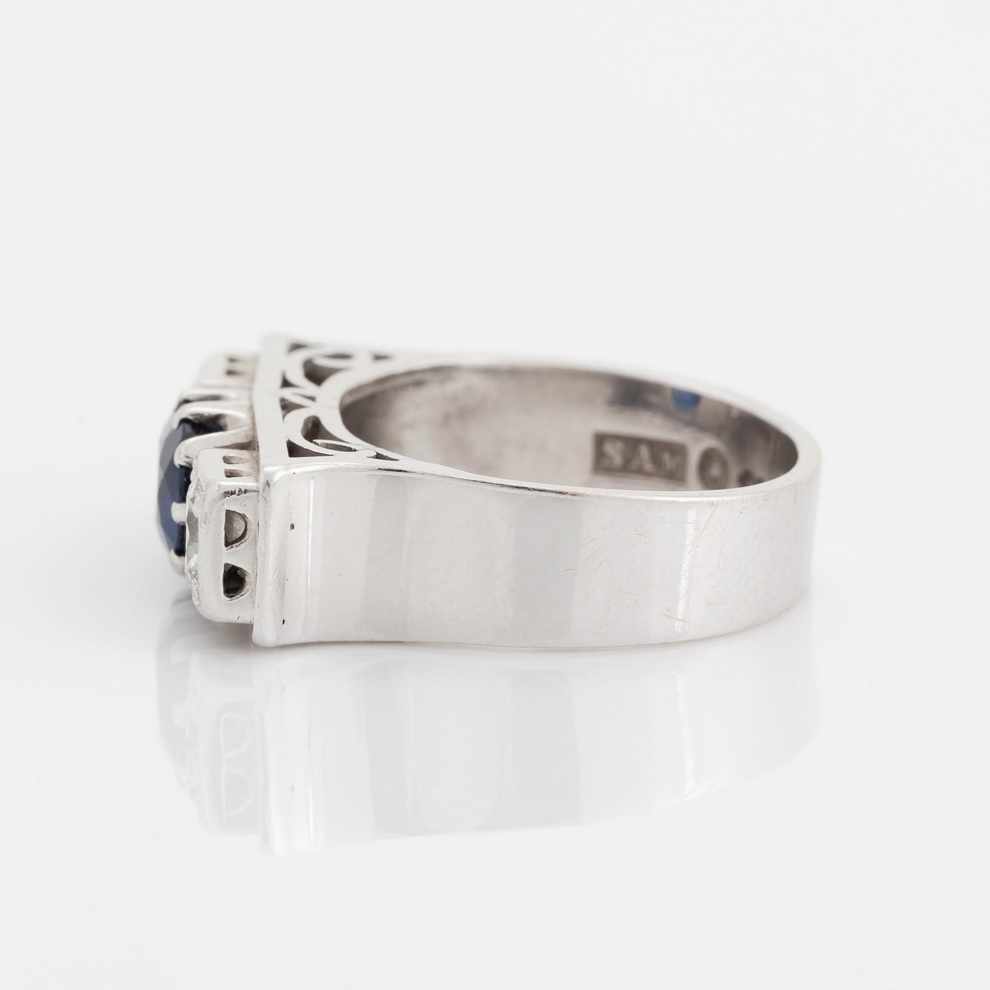 An 18K white gold ring set with a faceted sapphire, possibly synthetic, and round brilliant-cut diamonds.