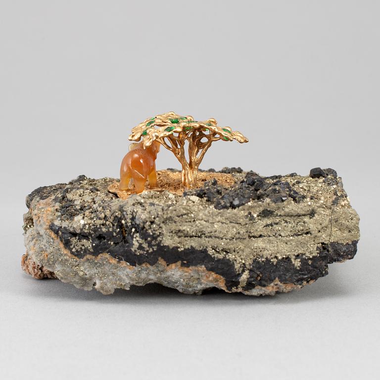 A sculpture of an agate elephant under a gilt three with inlays of tsavorites on rock formation, unmarked, 20th Century.