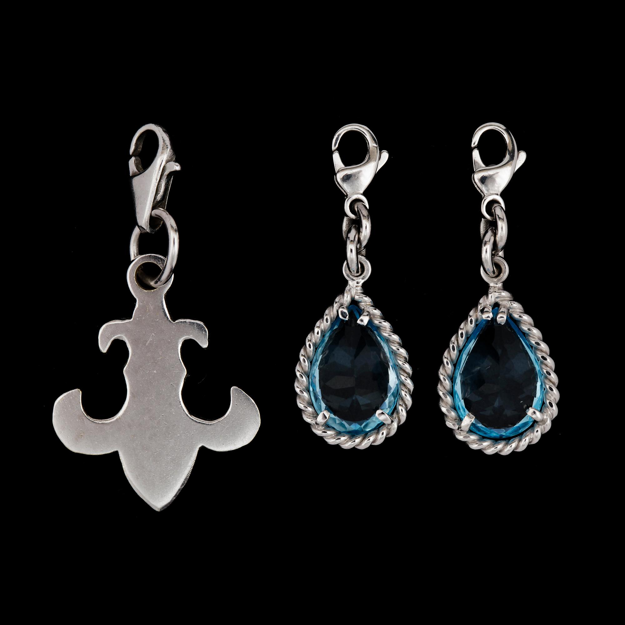 Two white gold and blue topas charms.