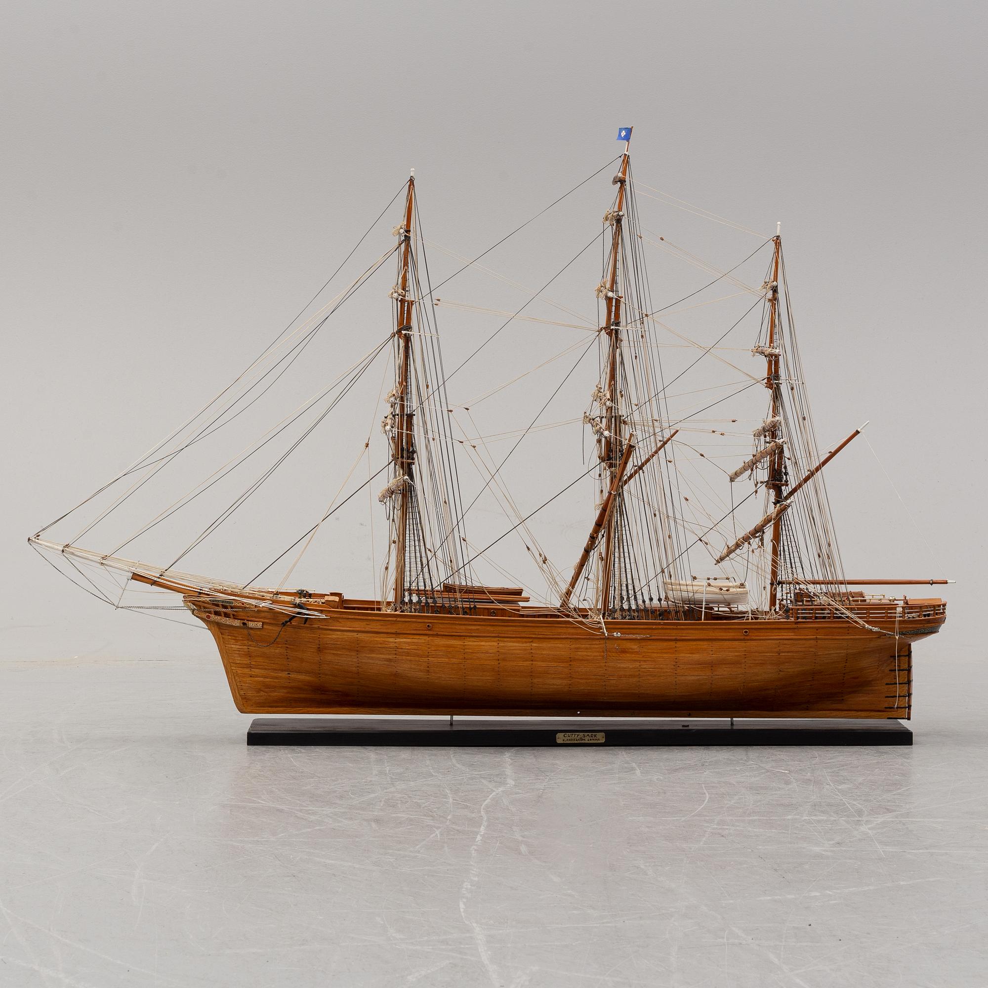 A wooden scale model of Cutty Sark on a painted wooden stand.