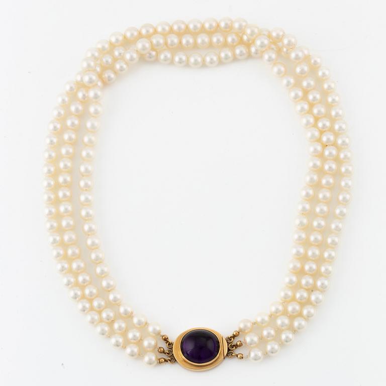 A three strand cultured pearls neckace clasp 18K gold with a purple stone, likely amethyst.