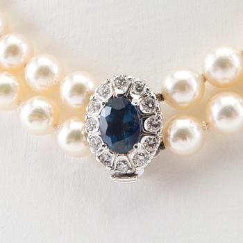 Halsband av odlade pärlor och lås i 18K vitt guld med en oval fasetterad safir samt runda briljantslipade diamanter.