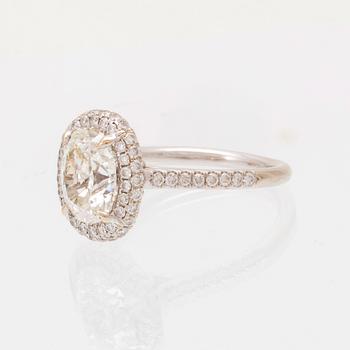 An 18K white gold ring by James Allen, set with an oval brilliant cut diamond in a halo of round brilliant cut diamonds.