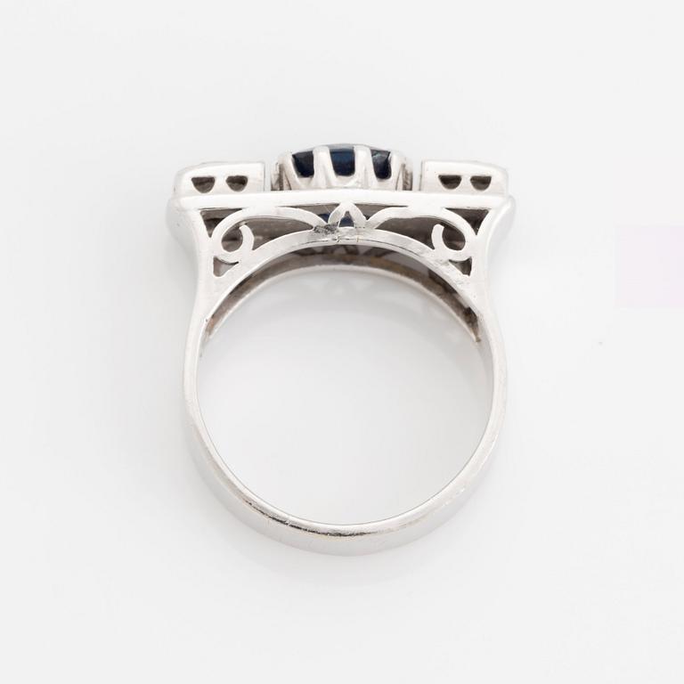 An 18K white gold ring set with a faceted sapphire, possibly synthetic, and round brilliant-cut diamonds.